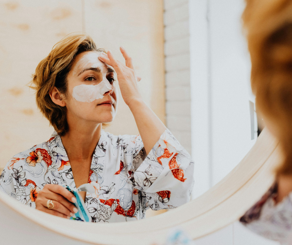 Woman applying skincare serum in bathroom mirror representing consistent medical-grade skincare routine for healthy skin
